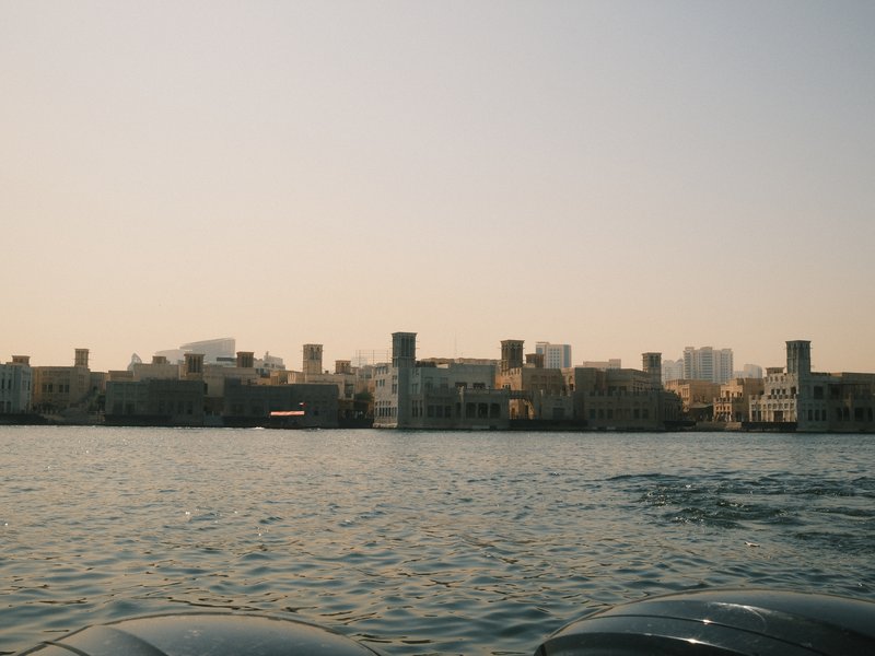 A panoramic view of a coastal city skyline with buildings and water in the foreground under a clear sky.