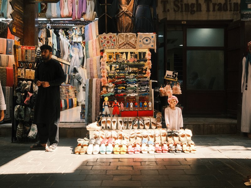 A bustling market scene with a vendor selling colorful trinkets and a child sitting on the ground.