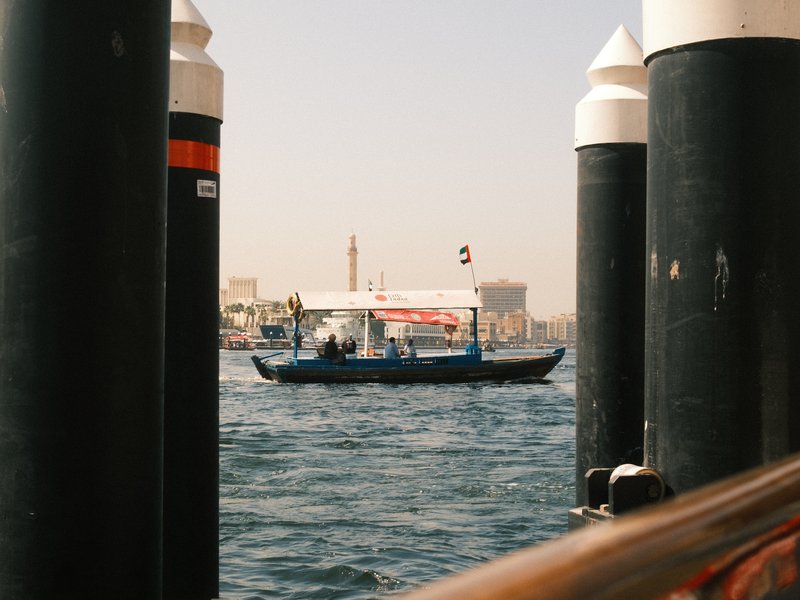 A small boat navigating through water, framed by dock pillars under a clear sky.