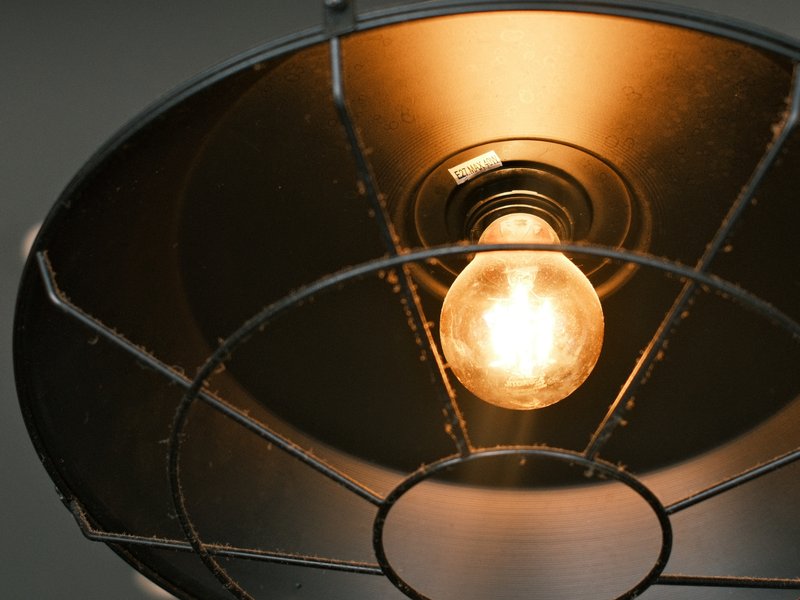 Close-up of a vintage light bulb inside a metal lampshade, glowing warmly.