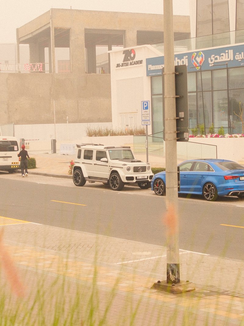 A street scene featuring parked cars, a person walking, and a building in a hazy atmosphere.