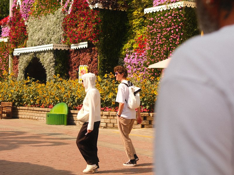 Two people walking in a vibrant floral park with colorful flowers in the background.