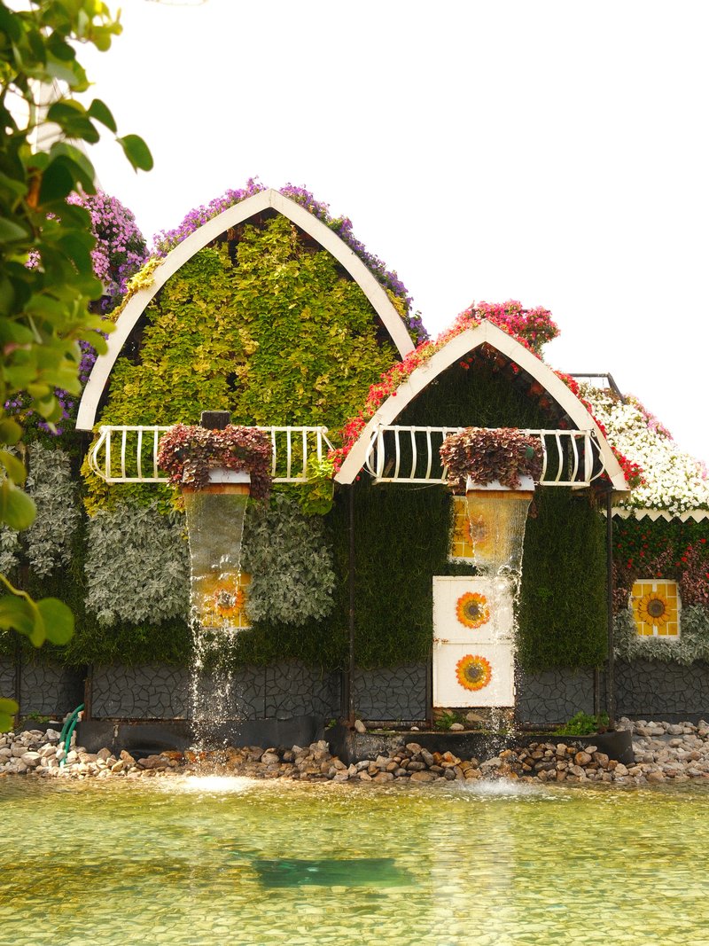 A vibrant floral house with greenery and colorful flowers, surrounded by water.
