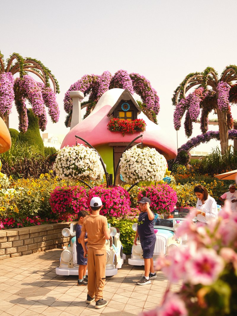 Colorful flower-covered houses with people enjoying the vibrant garden scene.