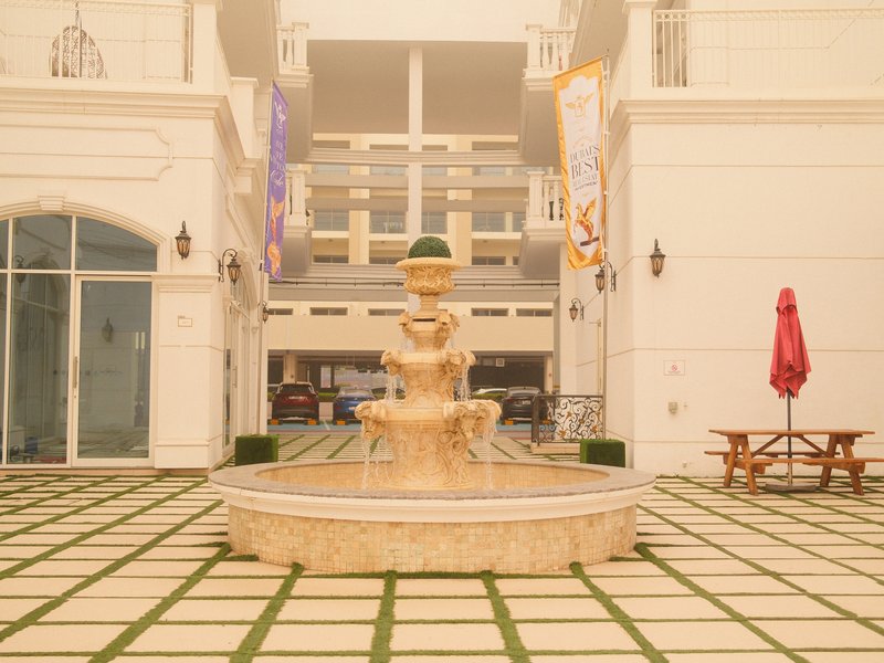 A fountain in a courtyard surrounded by white buildings and a red umbrella table.