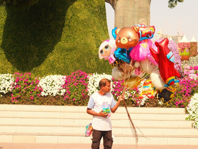 A child holding colorful balloons in a vibrant garden setting with flowers in the background.