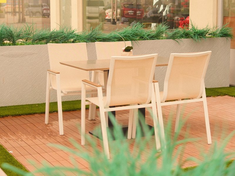 A small outdoor dining area with white chairs and a table surrounded by green grass-like plants.