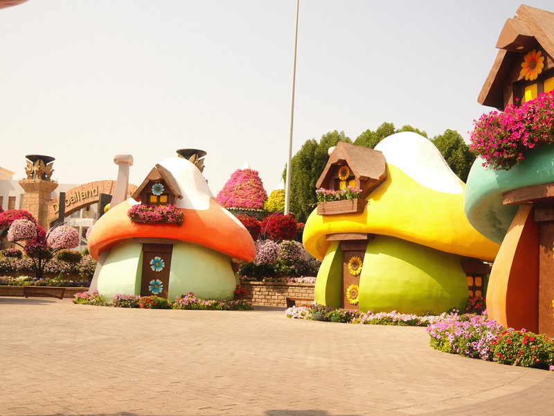 Colorful mushroom-shaped houses surrounded by flowers in a sunny outdoor setting.
