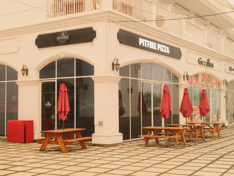 A pizza restaurant with red umbrellas and outdoor seating in a bright, sunny setting.