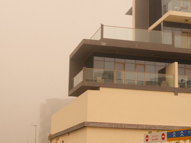 A modern building corner with glass balconies, partially obscured by dust in a hazy atmosphere.