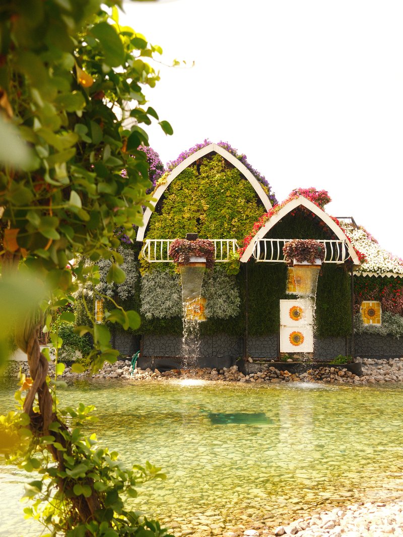 A charming floral house surrounded by water and greenery, with vibrant flowers adorning the structure.