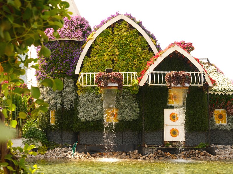 A whimsical house covered in vibrant flowers and greenery, showcasing a unique architectural design.