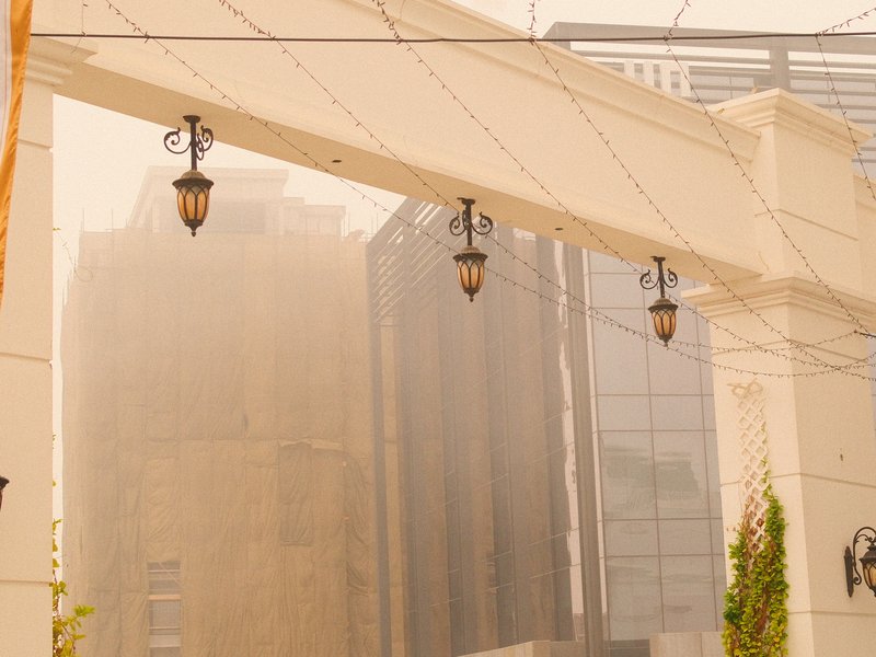 A hazy urban scene featuring buildings obscured by dust, with decorative lamps hanging overhead.