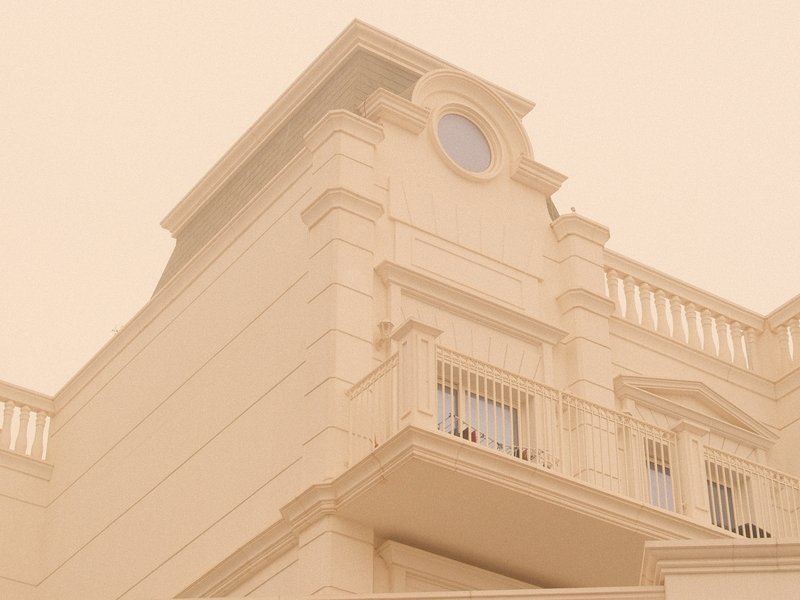 A pale building with a circular window and balcony under a hazy sky.