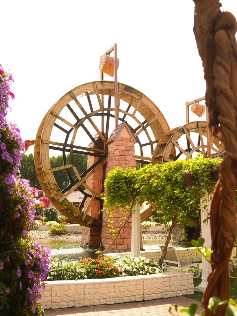 Two large wooden waterwheels surrounded by vibrant flowers and greenery in a garden setting.