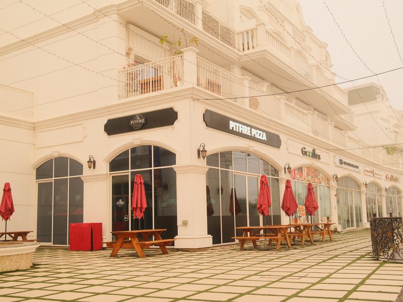 A white building with large glass windows and red umbrellas on tables in a foggy setting.