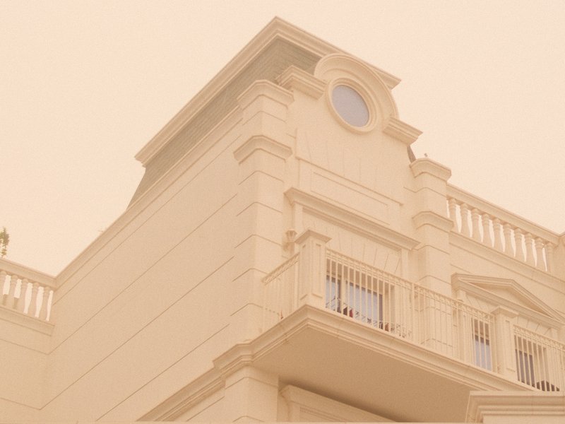 A close-up view of a light-colored building with a circular window and balcony under a hazy sky.