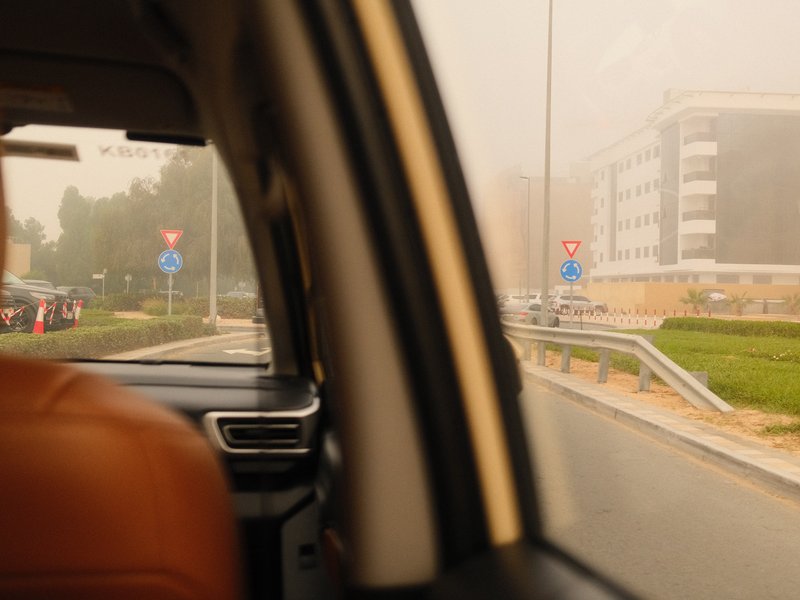 View from inside a car showing a foggy street with traffic signs and buildings in the background.
