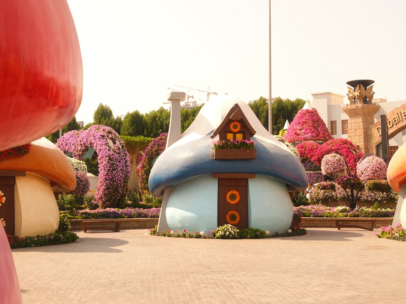 Colorful mushroom-shaped houses surrounded by vibrant flowers in a garden setting.