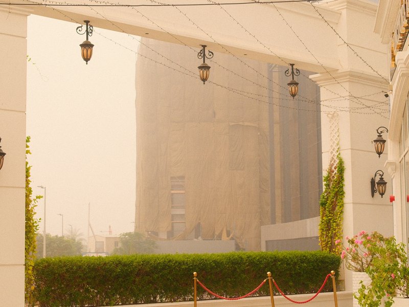 View of a large building partially obscured by haze, framed by decorative architecture and greenery.