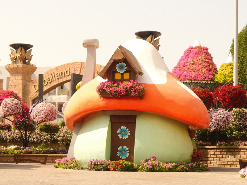 A whimsical mushroom-shaped house surrounded by colorful flowers in a garden setting.