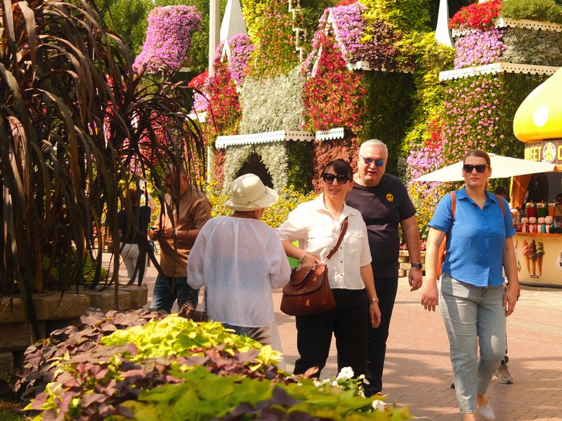 A vibrant scene of people walking through a colorful garden with floral decorations.