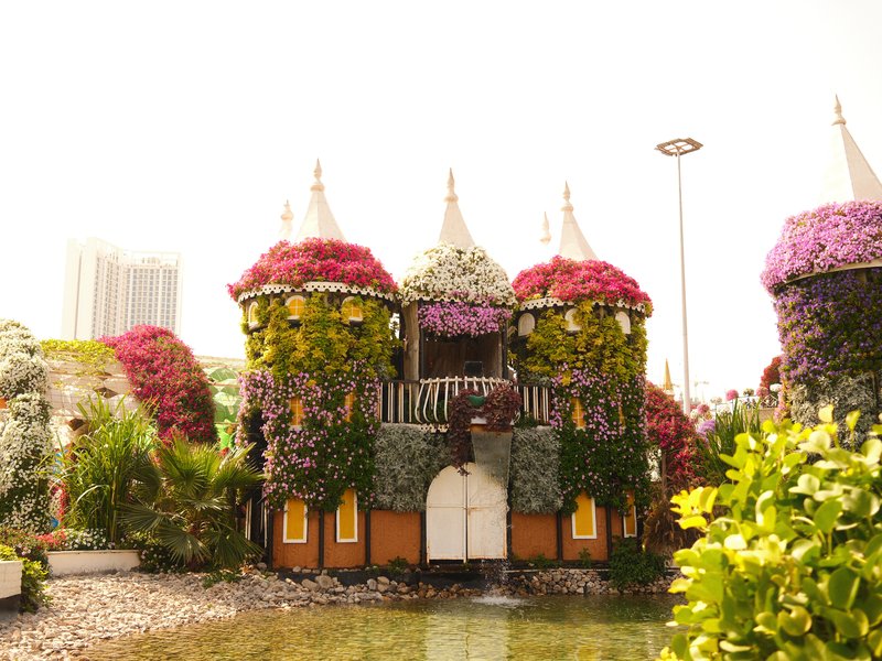 A whimsical floral castle surrounded by vibrant flowers and greenery under bright sunlight.