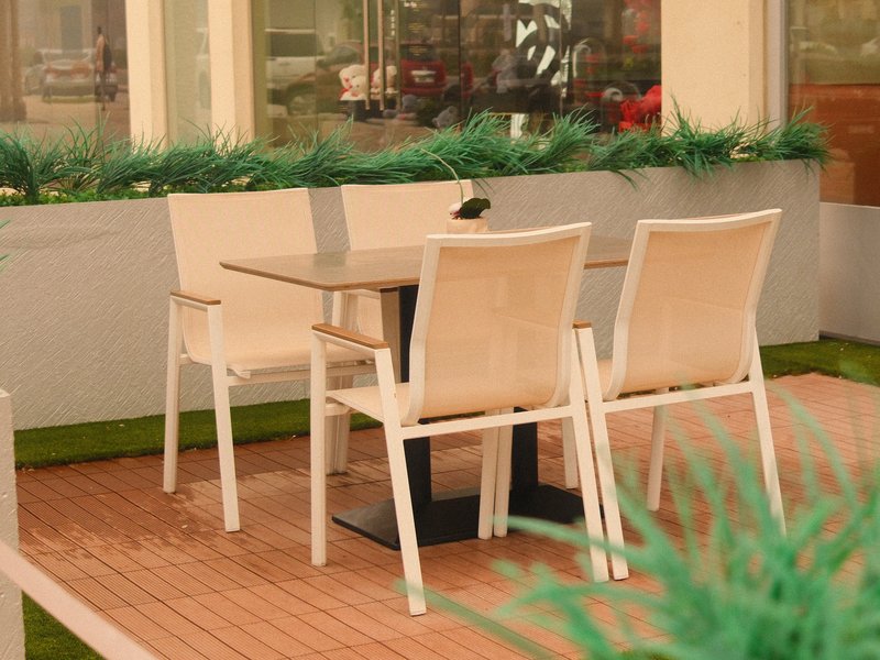 A small outdoor dining area with two white chairs and a table surrounded by greenery.