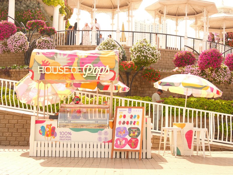 Colorful ice cream stand with umbrellas and flowers in a sunny outdoor setting.