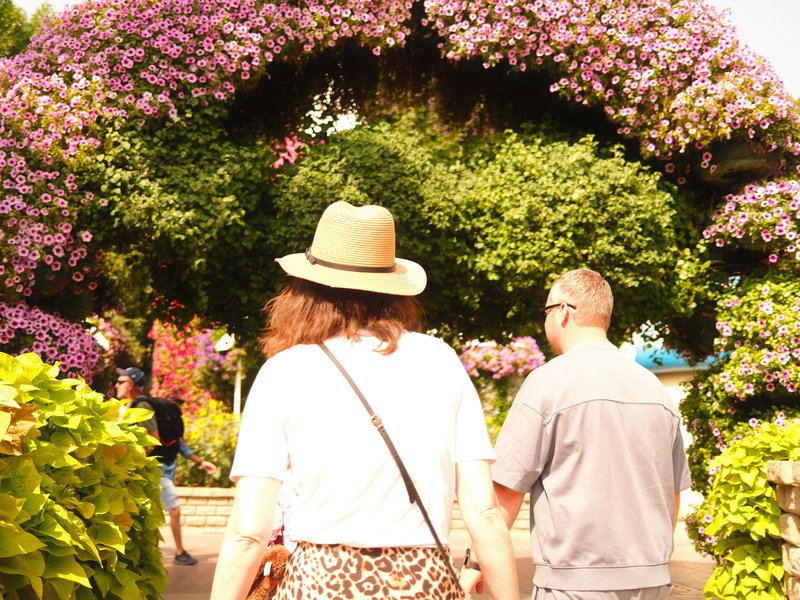 Two people walking through a floral archway in a vibrant garden setting.