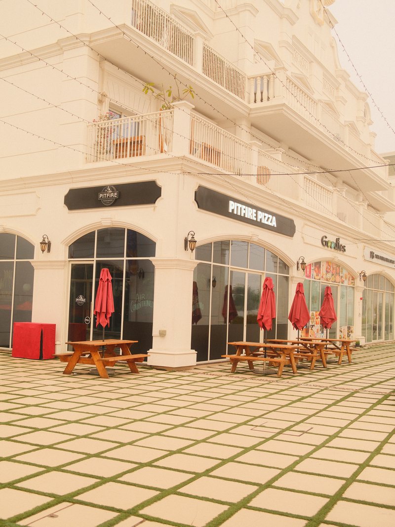 Outdoor cafe with red umbrellas and wooden tables in front of a white building.