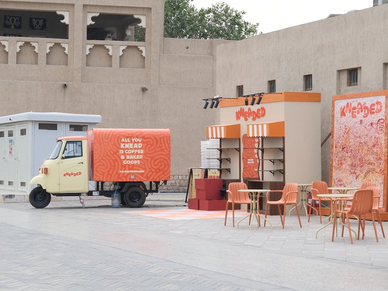 A colorful food truck and kiosk in an urban setting with outdoor seating.