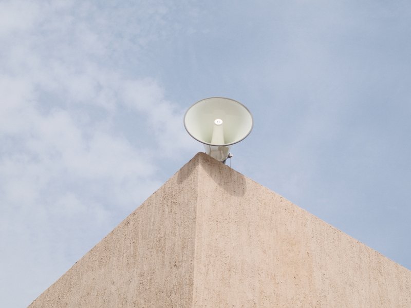 A light fixture mounted on the corner of a beige building against a blue sky with scattered clouds.