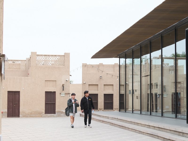 Two people walking in a modern architectural setting with a glass facade and traditional buildings.