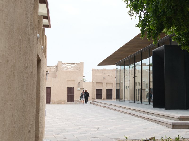 Two people walking towards a modern glass building in a historic urban setting.