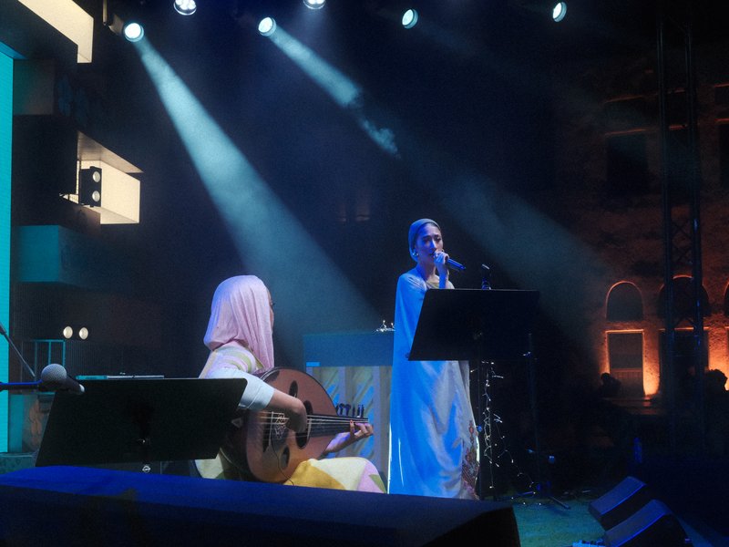Two musicians performing on stage with dramatic lighting and a colorful backdrop.