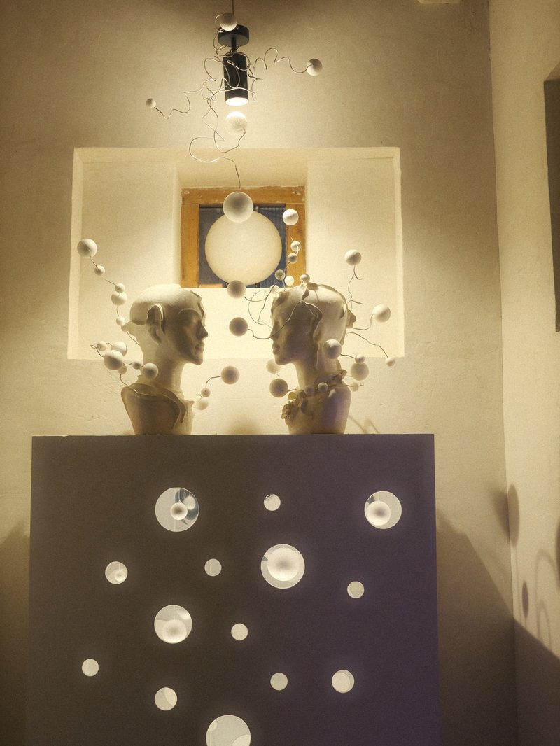 Two sculpted heads facing each other on a pedestal, surrounded by decorative elements and soft lighting.