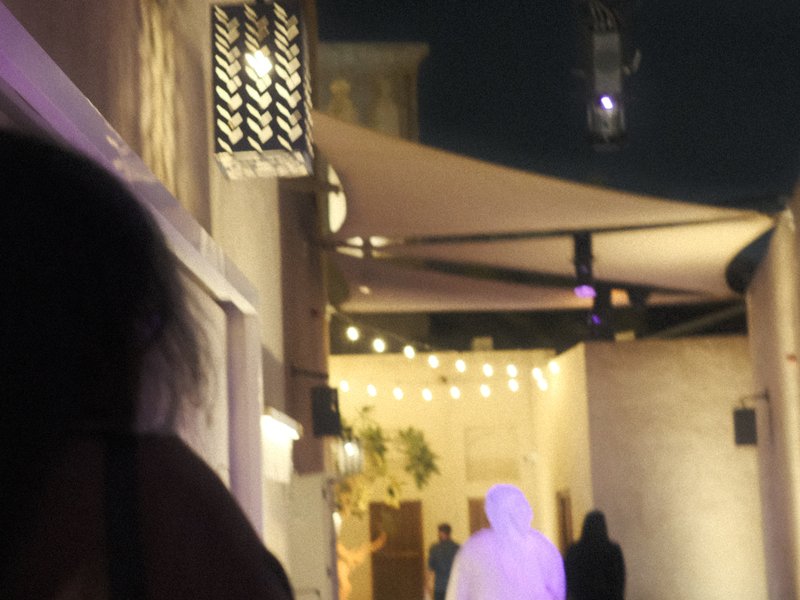 A dimly lit alleyway with people walking, adorned with decorative lanterns and fabric canopies.