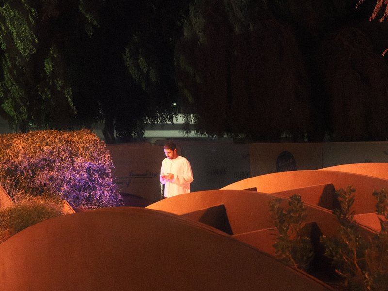 A person in a white shirt stands among curved, orange structures at night, illuminated by soft light.