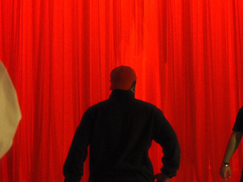Silhouetted figures in front of a bright red curtain, creating a dramatic atmosphere.