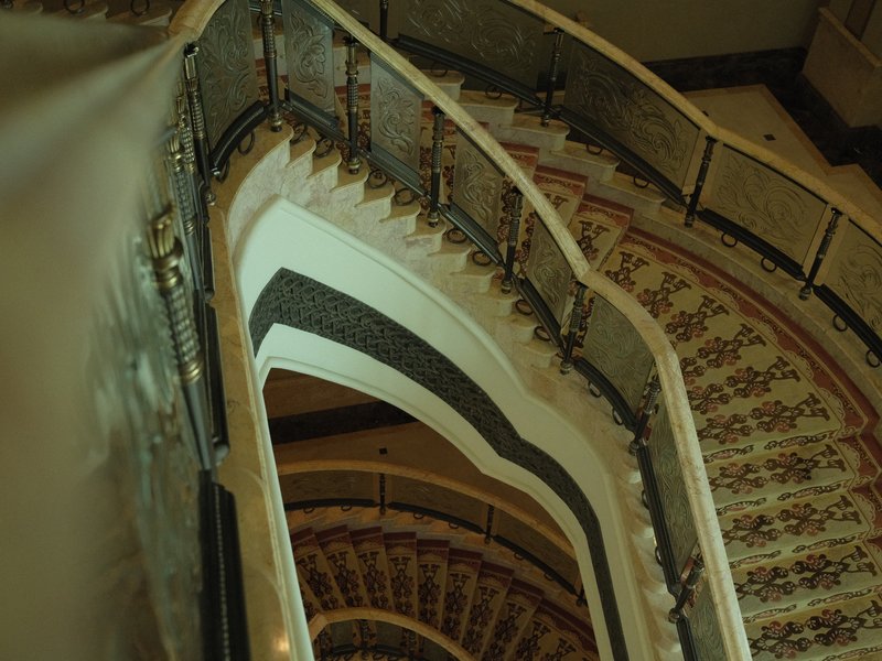 A spiral staircase with ornate railings and patterned carpet, viewed from above.