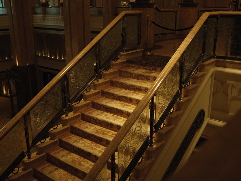 Elegant staircase with wooden railings and marble steps, softly lit in a grand indoor setting.