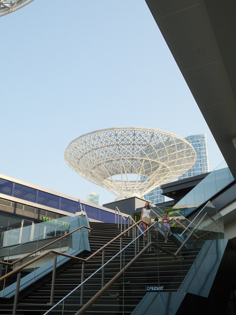 Modern architectural structure with a large canopy above a staircase in an urban setting.