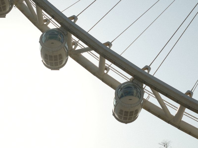 Close-up of a ferris wheel with several cabins against a bright sky.