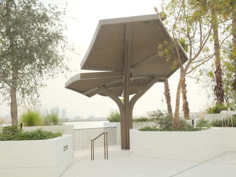 A modern pavilion structure surrounded by greenery and palm trees in a serene outdoor setting.