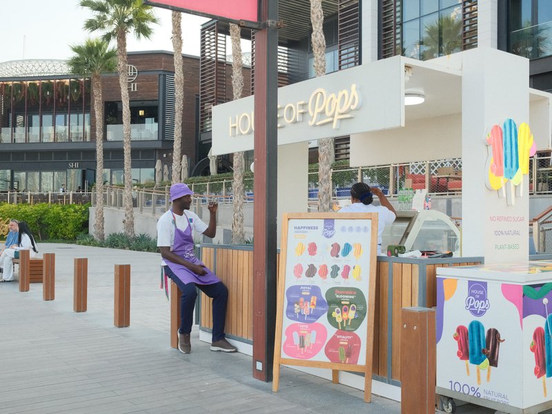 A colorful ice cream stand with a vendor serving customers in a sunny outdoor setting.