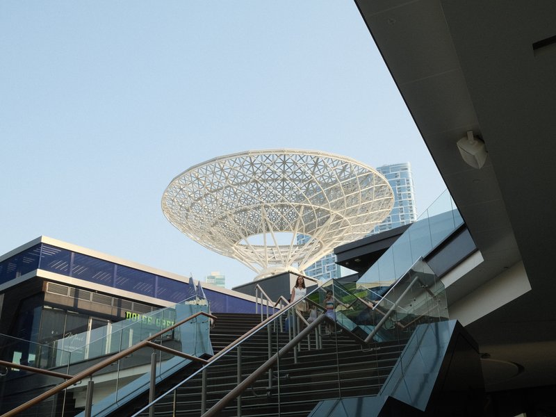 A modern architectural structure resembling a large flower, surrounded by buildings and a clear sky.