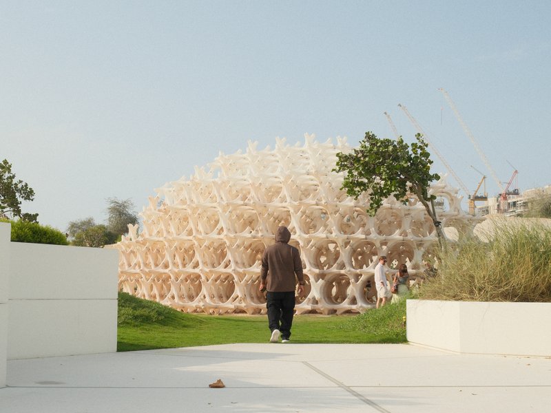 A person walking towards a large, intricate architectural structure surrounded by greenery.