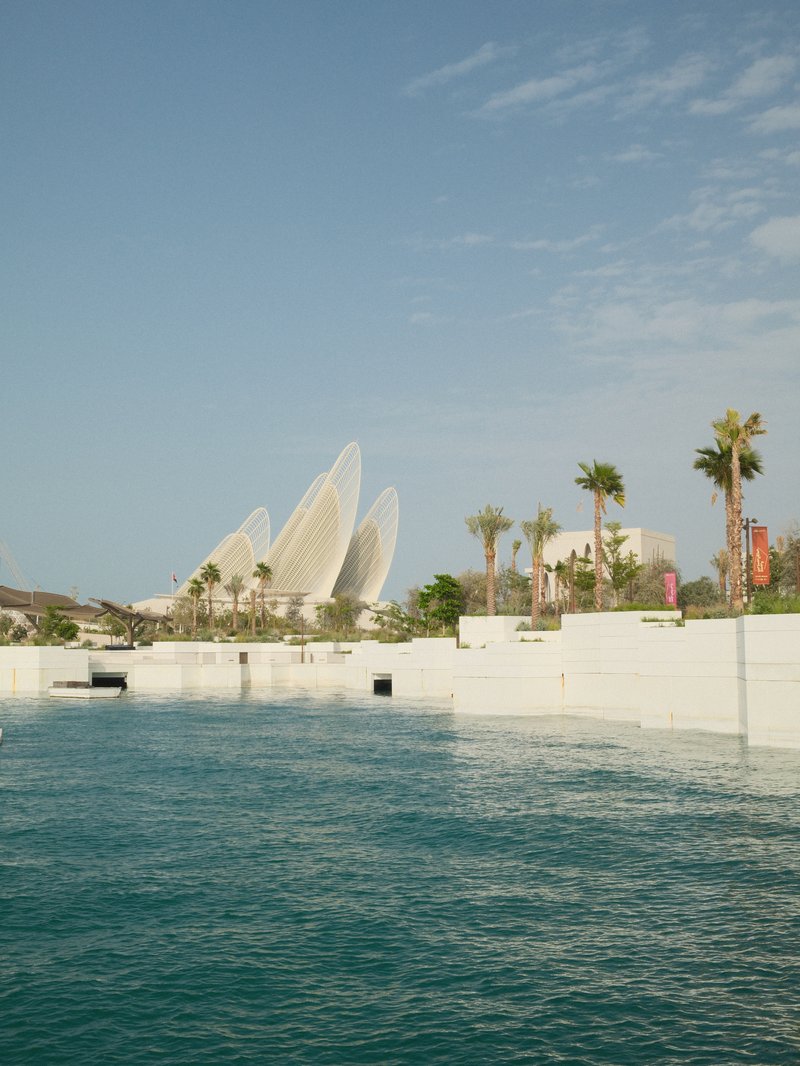 A modern architectural structure resembling sails near a body of water, with palm trees and a clear sky.