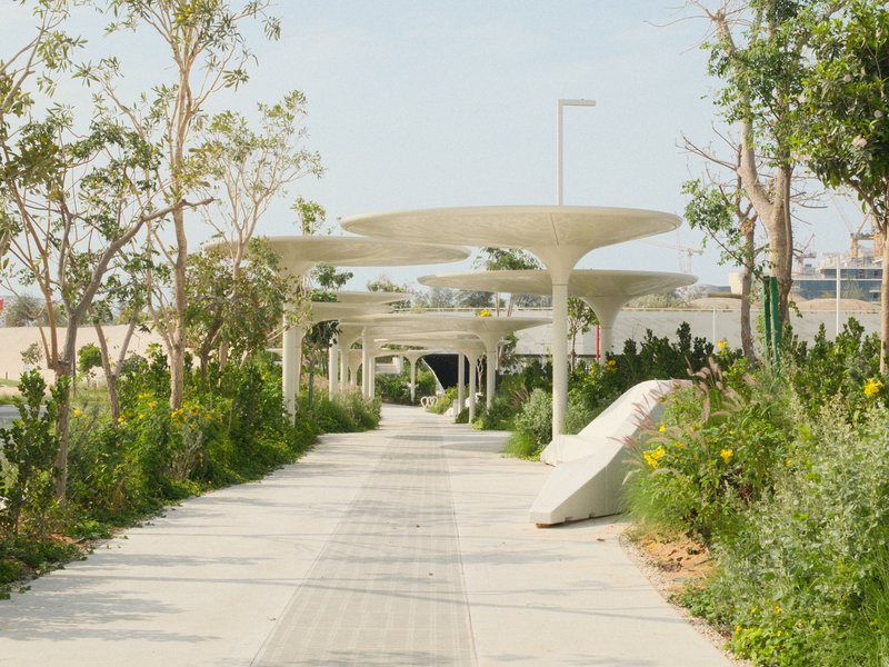 A modern pathway lined with greenery and unique architectural structures in a sunny outdoor setting.